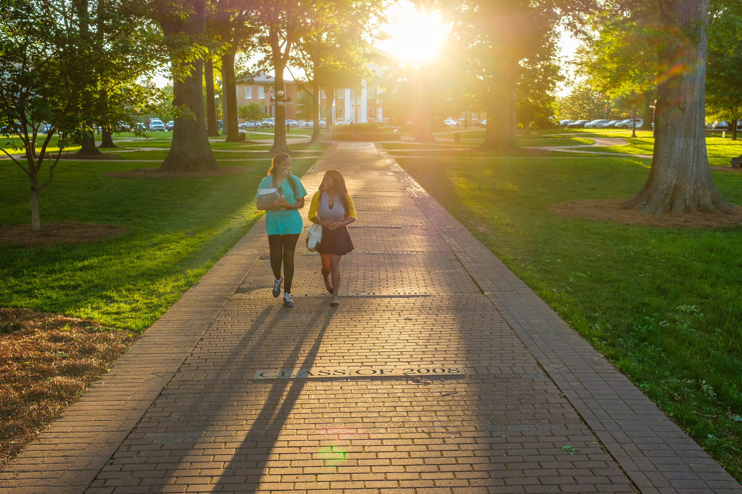 Two students walking through the grove on campus with the sun in the backdrop